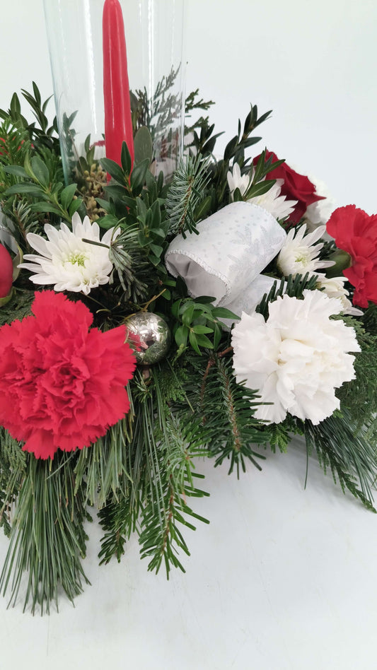 Candlelit Christmas arrangement with flowers, red taper candle, evergreens, and festive accents.