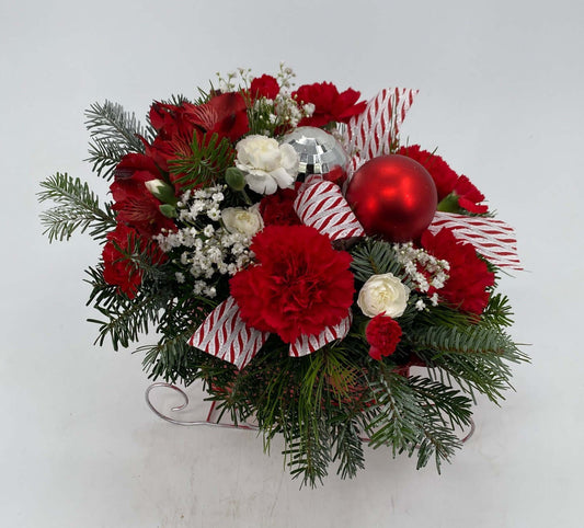 Sleighride Splendor arrangement featuring red and white flowers, festive ribbon, and evergreens for holiday cheer.