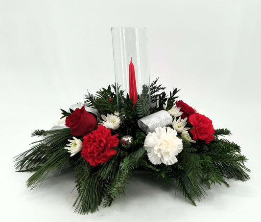 Candlelit Christmas arrangement featuring red roses, white daisies, and a glowing taper candle in a festive centerpiece.